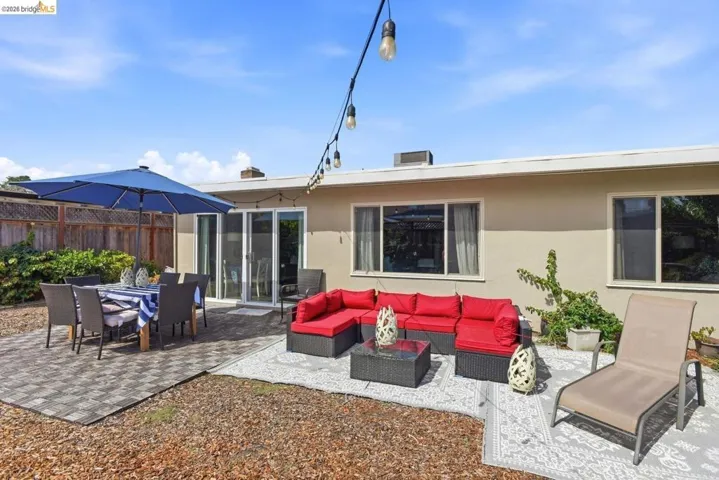 Spacious outdoor patio area with multiple seating zones, paver stone section, sliding glass doors, and string lighting