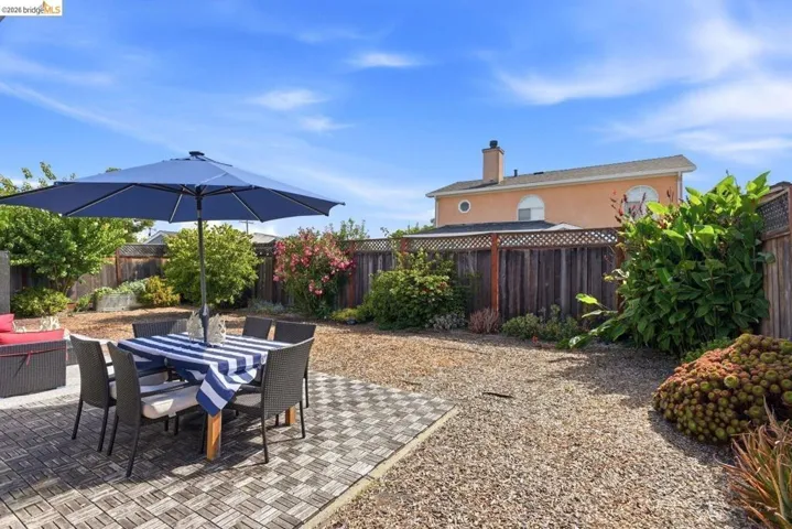 Spacious backyard featuring a tiled patio area, gravel landscaping, wood fencing, and mature plantings