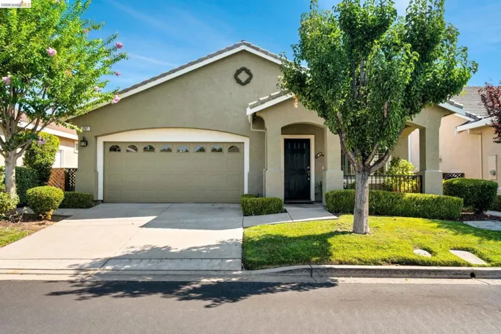 Stucco exterior with a pitched roof, attached garage with arched window inserts, concrete driveway, and covered entryway with a dark paneled door