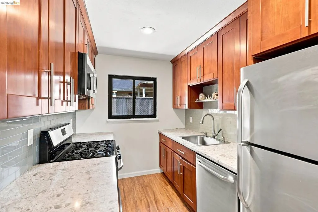 Kitchen featuring wood-finish cabinetry, light-toned countertops, a stainless steel sink, a tile backsplash, and wood-finish flooring