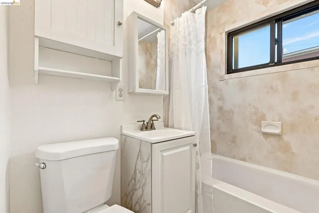Bathroom featuring a white vanity with an integrated sink, a built-in medicine cabinet, and a window above the bathtub