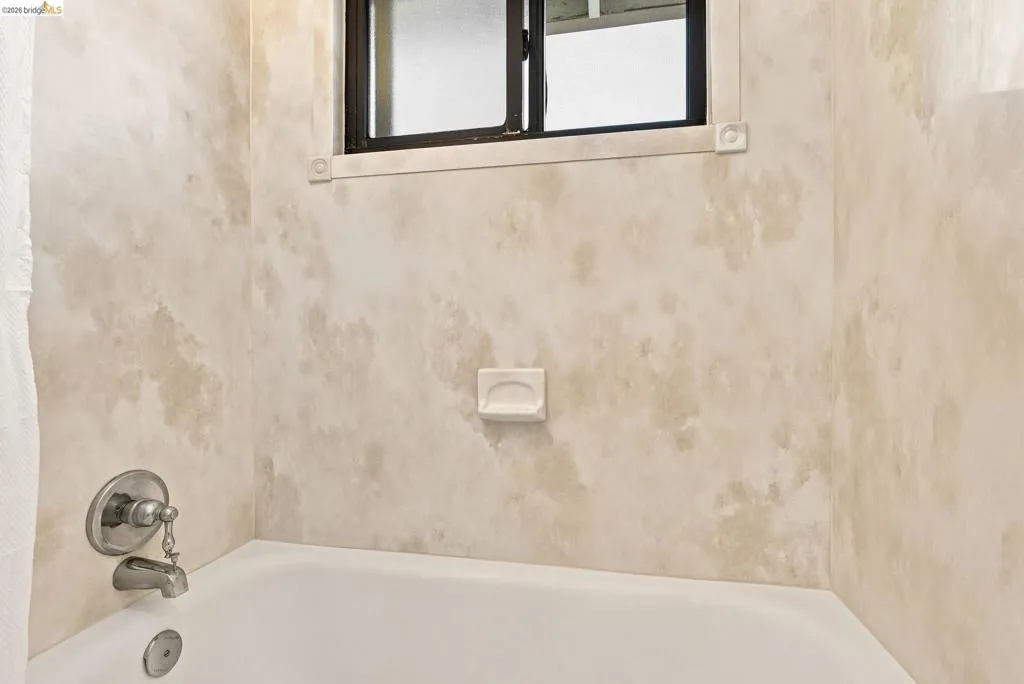 Bathtub with a brushed nickel faucet, a soap dish, and a window with frosted glass