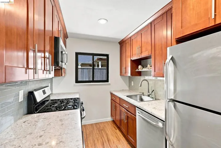 Kitchen featuring wood-finish cabinetry, light-toned countertops, a stainless steel sink, a tile backsplash, and wood-finish flooring