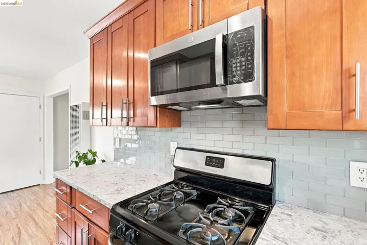 Wood-finish cabinetry, stainless steel microwave, gas range, light-toned countertop, and light-toned subway tile backsplash
