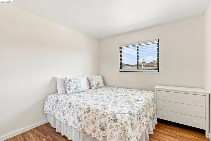 Wood-finish flooring, white walls, and a window with horizontal blinds
