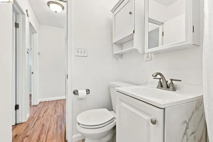 Bathroom featuring a white vanity with integrated sink, brushed nickel faucet, wall-mounted medicine cabinet, and wood-finish flooring