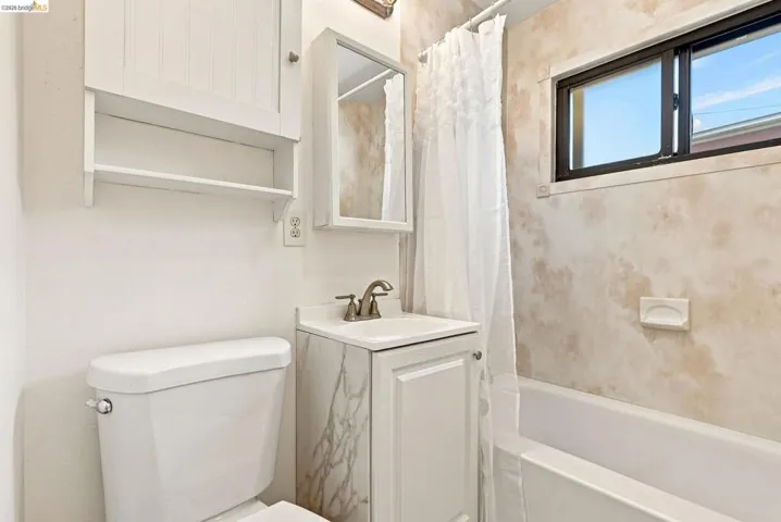 Bathroom featuring a white vanity with an integrated sink, a built-in medicine cabinet, and a window above the bathtub