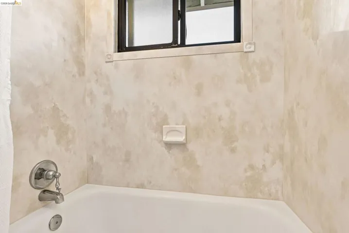 Bathtub with a brushed nickel faucet, a soap dish, and a window with frosted glass