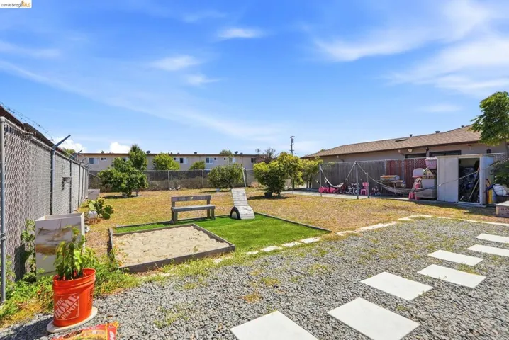 Expansive backyard featuring a gravel-covered area, concrete stepping stones, and a chain-link fence
