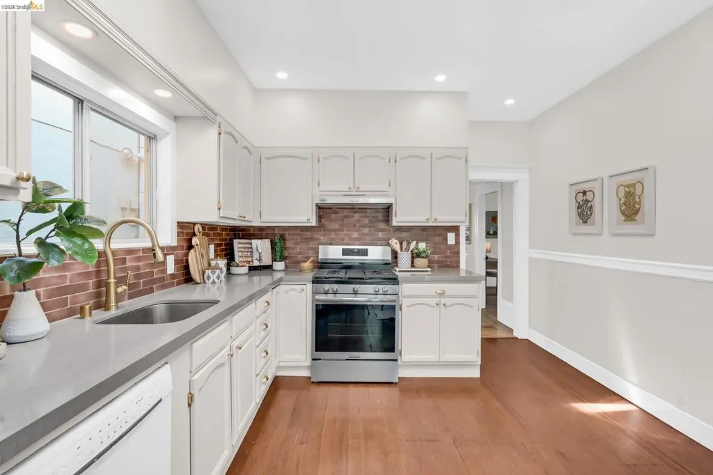 Kitchen featuring white cabinetry, gray countertops, stainless steel gas range, and a brick-patterned backsplash