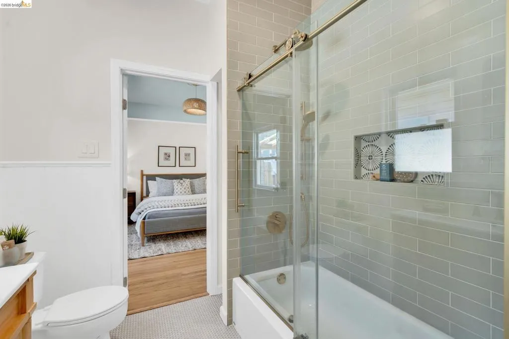 Tub and shower combination with a glass sliding door, subway tile surround, recessed shelf with mosaic tile, and brushed brass fixtures