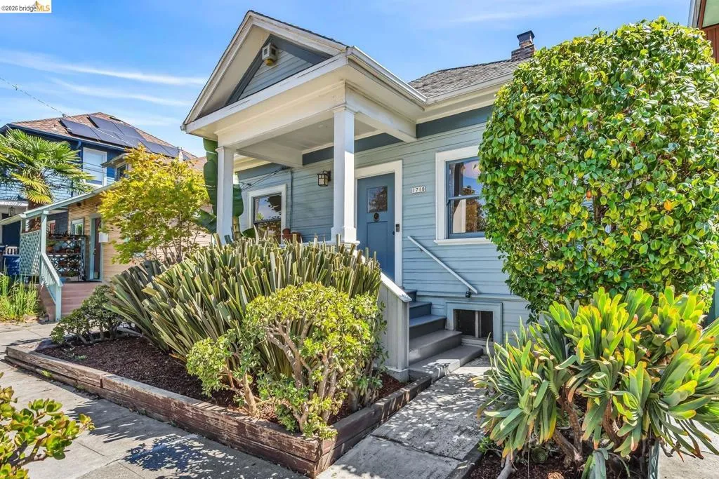Light blue exterior with white trim, covered front porch, grey entry door, concrete steps, and established landscaping
