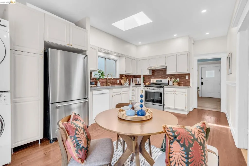 Hardwood-style flooring, stainless steel appliances, brick-style backsplash, and a skylight