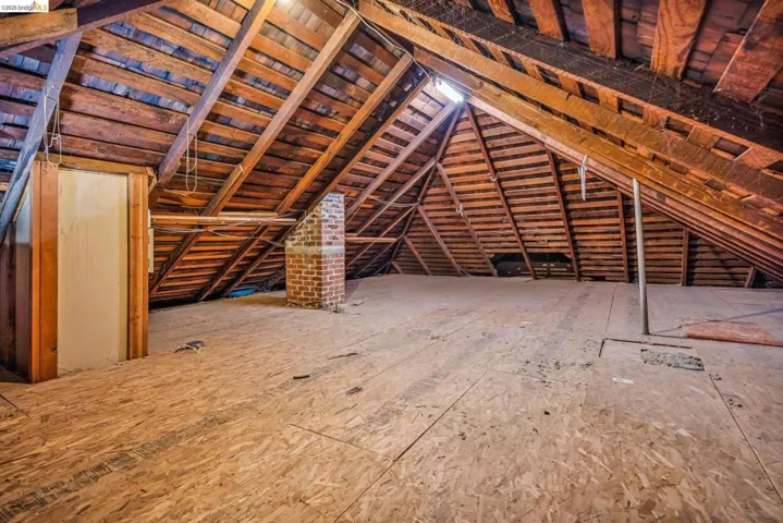 Unfinished attic space featuring exposed wood rafter system, brick chimney, and plywood flooring