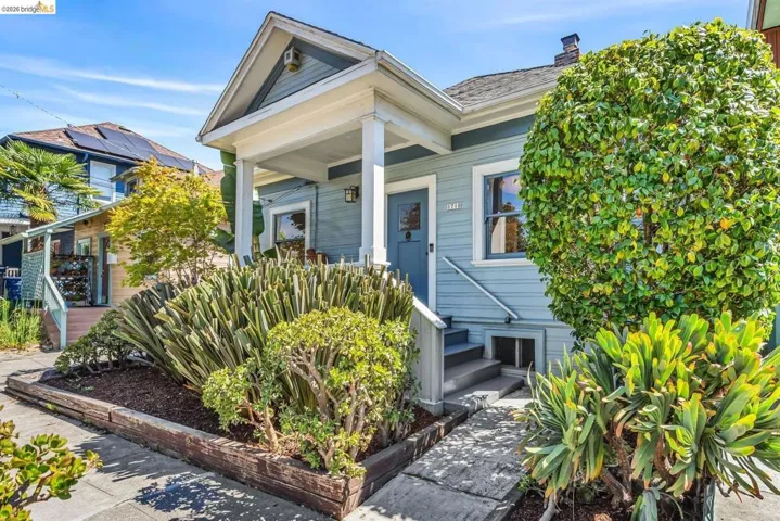 Light blue exterior with white trim, covered front porch, grey entry door, concrete steps, and established landscaping