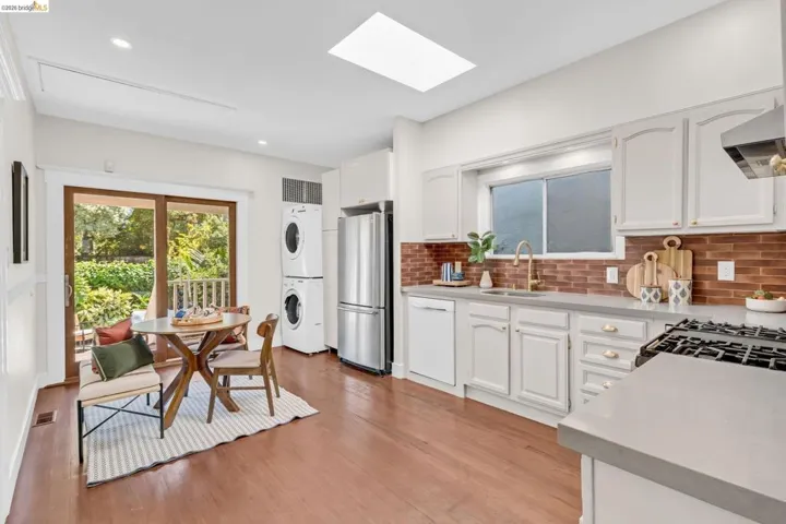 Hardwood flooring, a large skylight, white cabinetry, a wood-finish backsplash, and stainless steel appliances