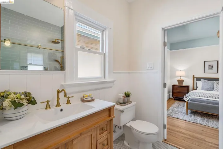 Bathroom featuring a wood-finish vanity with a white countertop and undermount sink, brass-finish faucet, and white wainscoting