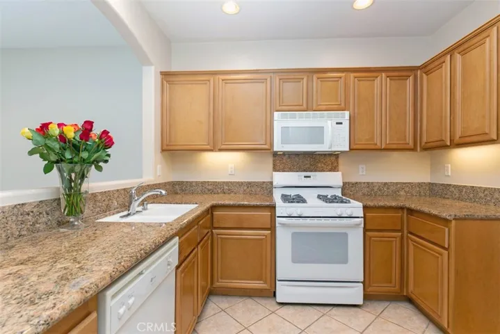Wraparound kitchen with slab granite countertops, maple cabinets, and white appliances. *flooring to be updated with LVP prior to move-in.