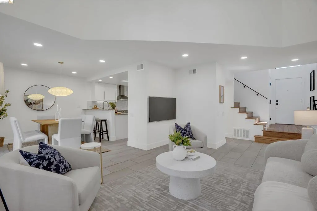 Open-concept living space featuring wood-finish flooring, recessed lighting, and a modern staircase with a dark handrail