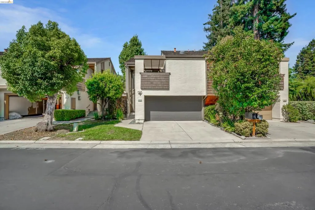 Stucco exterior with wood shake accents, attached garage, and mature landscaping