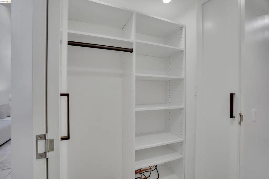 Built-in closet system featuring white shelving, a dark-finish hanging rod, and recessed lighting