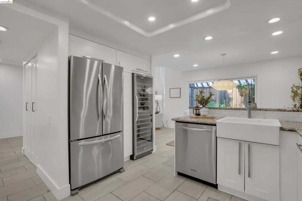 Kitchen featuring recessed lighting, a white farmhouse sink, stainless steel appliances, white cabinetry, and light-toned tile flooring