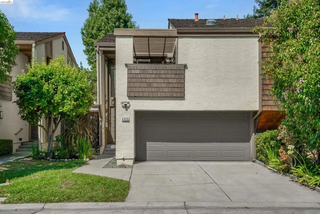 Stucco exterior with cedar shake accents, attached garage with a paved driveway, and mature landscaping