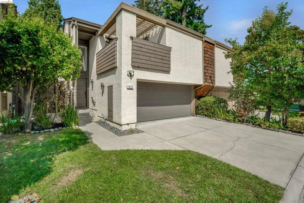 Stucco exterior with wood-shingle accents, attached garage, concrete driveway, and front entryway