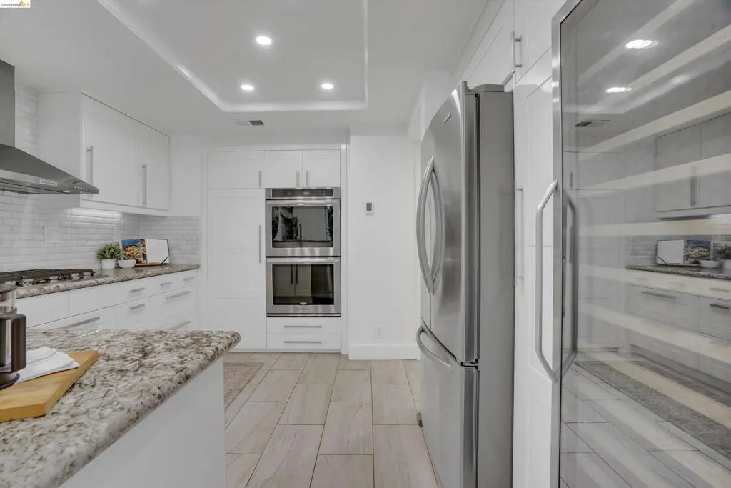 White cabinetry, stainless steel appliances, granite countertops, tile backsplash, and wood-finish flooring