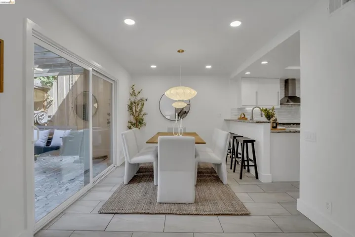 Recessed lighting and a modern pendant light illuminate the dining area, featuring light tile flooring and a sliding glass door