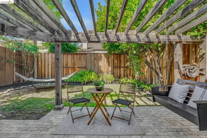 Paved patio with an overhead wooden pergola, enclosed by a privacy fence, and featuring a manicured lawn
