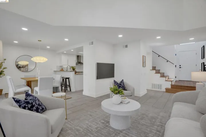Open-concept living space featuring wood-finish flooring, recessed lighting, and a modern staircase with a dark handrail