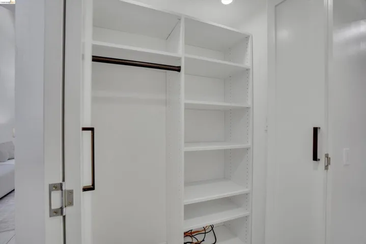 Built-in closet system featuring white shelving, a dark-finish hanging rod, and recessed lighting