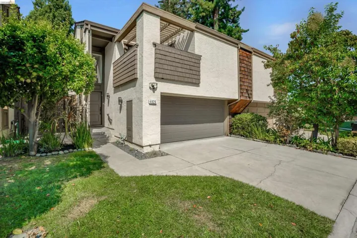 Stucco exterior with wood-shingle accents, attached garage, concrete driveway, and front entryway