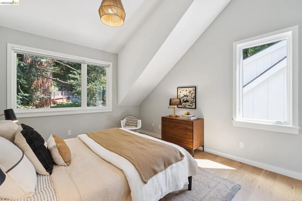 Slanted ceiling room featuring a large window, a smaller vertical window, wood-finish flooring, and a built-in light fixture Slanted ceiling room featuring a large window, a smaller vertical window, wood-finish flooring, and a built-in light fixture