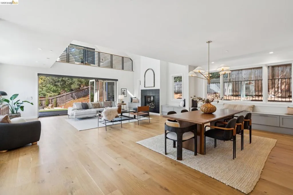 Expansive open-concept living area featuring wood-finish flooring, a contemporary fireplace with dark tile surround, and a dining area with a modern chandelier Expansive open-concept living area featuring wood-finish flooring, a contemporary fireplace with dark tile surround, and a dining area with a modern chandelier