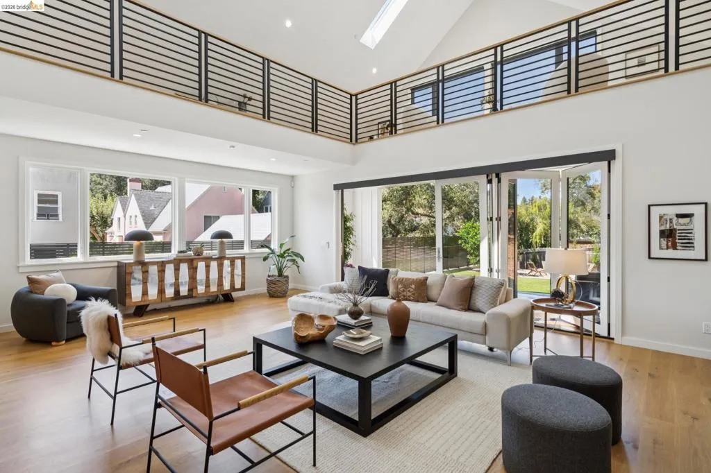 Vaulted ceilings with a prominent skylight, wood-finish flooring, a full wall of bi-fold glass doors, and an open-concept upper-level balcony with metal railing Vaulted ceilings with a prominent skylight, wood-finish flooring, a full wall of bi-fold glass doors, and an open-concept upper-level balcony with metal railing