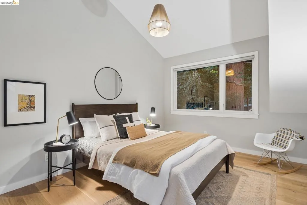 Vaulted ceiling with an overhead light fixture, large window, wood-finish flooring, and a built-in wall niche Vaulted ceiling with an overhead light fixture, large window, wood-finish flooring, and a built-in wall niche