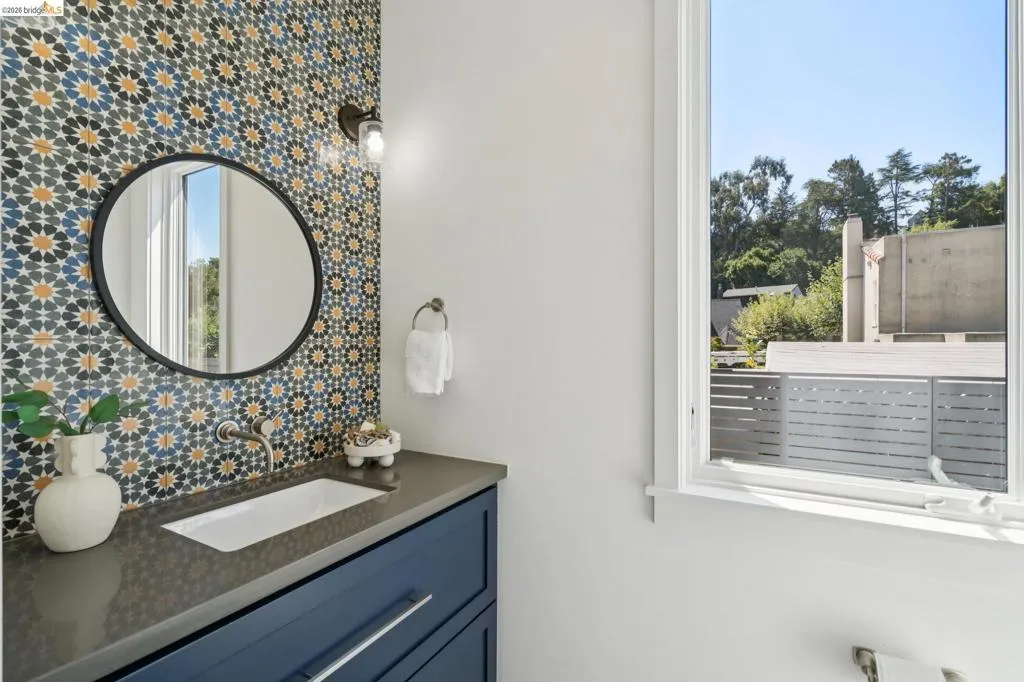 Patterned accent wall tiling, dark blue vanity with drawer storage, rectangular undermount sink, wall-mounted faucet, and a large window Patterned accent wall tiling, dark blue vanity with drawer storage, rectangular undermount sink, wall-mounted faucet, and a large window