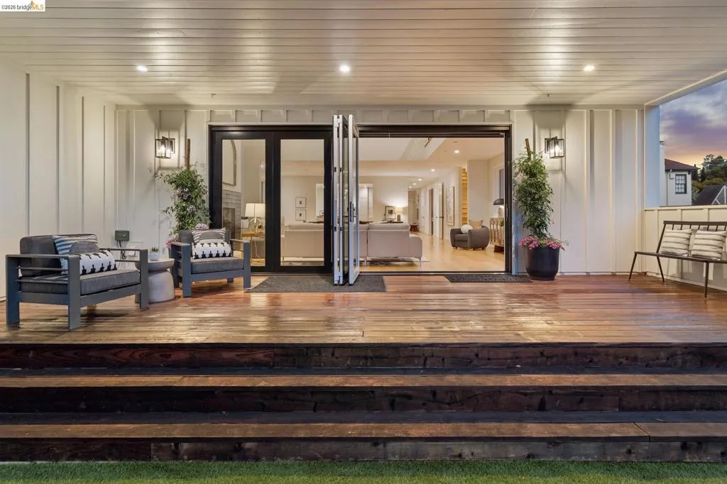 Expansive outdoor deck with wood flooring and multi-level steps, featuring black framed bi-fold doors, white paneled walls, and recessed lighting Expansive outdoor deck with wood flooring and multi-level steps, featuring black framed bi-fold doors, white paneled walls, and recessed lighting