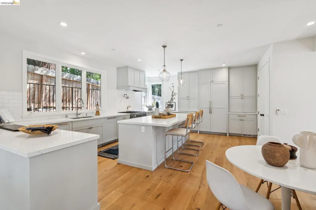 Kitchen featuring wood-finish flooring, light grey cabinetry, white countertops, a large center island, and an integrated refrigerator Kitchen featuring wood-finish flooring, light grey cabinetry, white countertops, a large center island, and an integrated refrigerator
