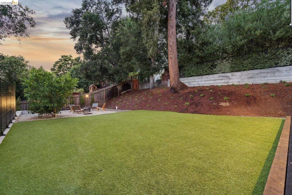 Expansive artificial turf lawn, gravel patio area, wood fencing, retaining wall, and mature landscaping Expansive artificial turf lawn, gravel patio area, wood fencing, retaining wall, and mature landscaping