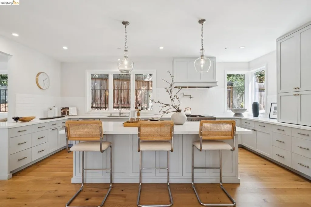 Spacious kitchen featuring a central island, light wood-finish flooring, white subway tile backsplash, and light-toned cabinetry with modern hardware Spacious kitchen featuring a central island, light wood-finish flooring, white subway tile backsplash, and light-toned cabinetry with modern hardware
