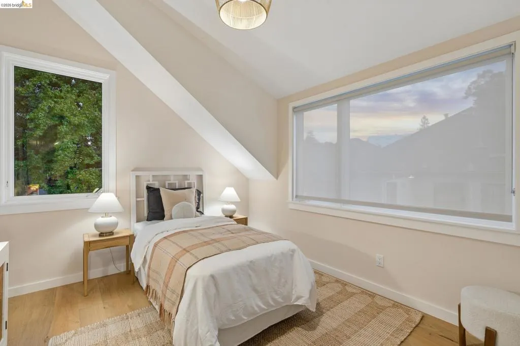Sloped ceilings, wood-finish flooring, and a large window with roller shades Sloped ceilings, wood-finish flooring, and a large window with roller shades