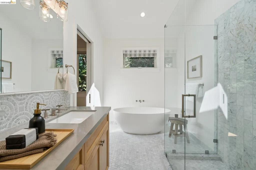 Freestanding soaking tub, walk-in shower with glass enclosure, wood vanity with integrated sink, patterned tile backsplash, and hexagonal floor tiles Freestanding soaking tub, walk-in shower with glass enclosure, wood vanity with integrated sink, patterned tile backsplash, and hexagonal floor tiles