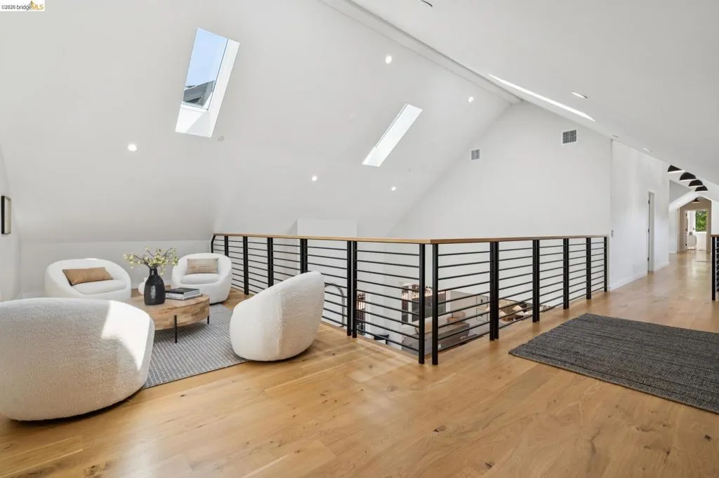 Vaulted ceiling with skylights, light wood-finish flooring, recessed lighting, and a modern horizontal railing with a wood-finish top Vaulted ceiling with skylights, light wood-finish flooring, recessed lighting, and a modern horizontal railing with a wood-finish top