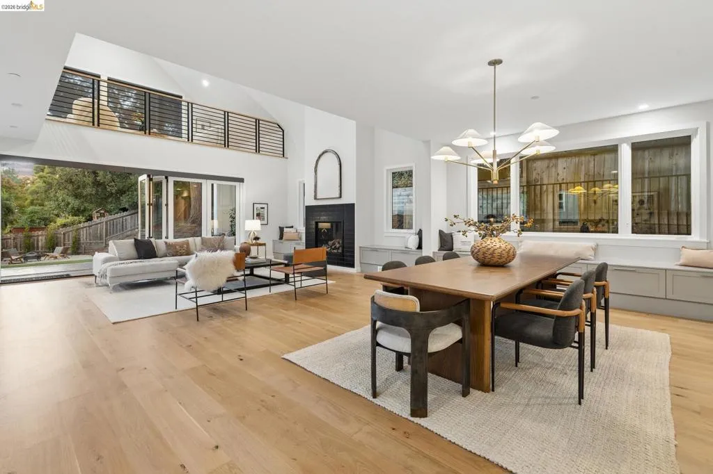 Spacious open-concept living area featuring light wood-finish flooring, a fireplace with a dark surround, and a two-story vaulted ceiling Spacious open-concept living area featuring light wood-finish flooring, a fireplace with a dark surround, and a two-story vaulted ceiling