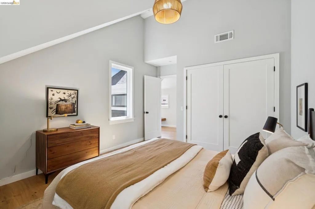 Vaulted ceiling with a woven pendant light, wood-finish flooring, white double-door closet, and white window trim Vaulted ceiling with a woven pendant light, wood-finish flooring, white double-door closet, and white window trim