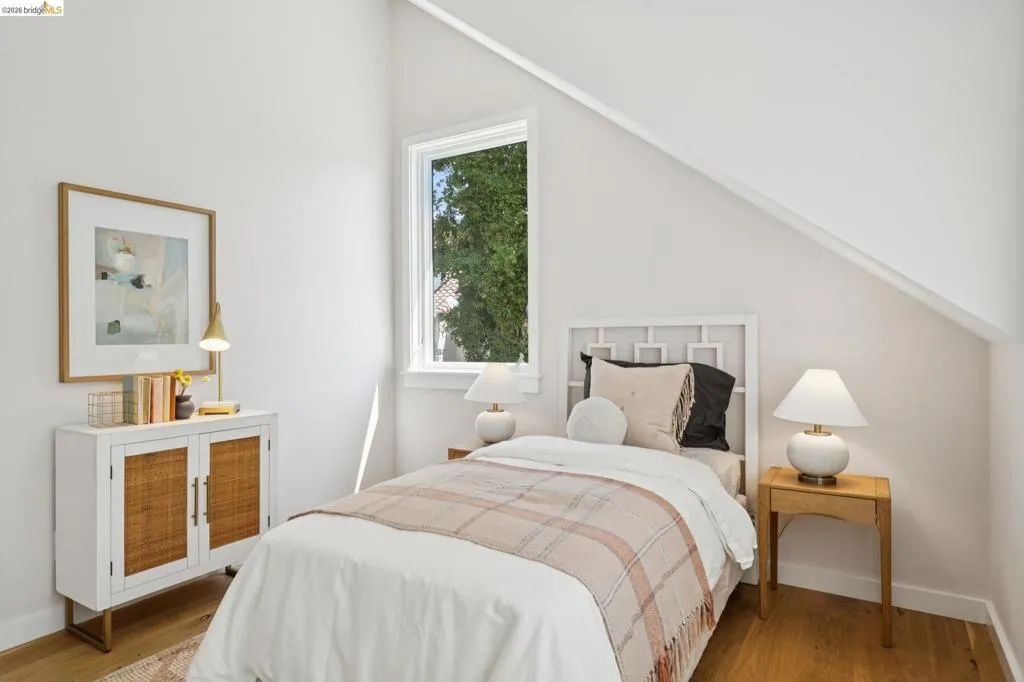 Hardwood flooring, white painted walls, white framed window, pitched ceiling, and a built-in storage cabinet with woven door panels Hardwood flooring, white painted walls, white framed window, pitched ceiling, and a built-in storage cabinet with woven door panels