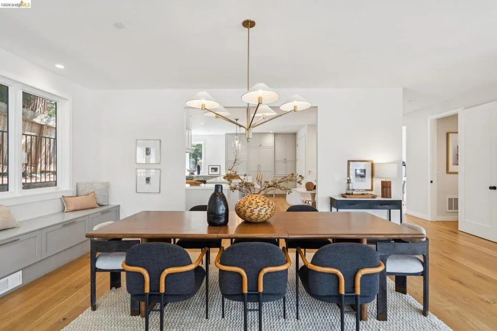 Open-concept dining area featuring wood-finish flooring, a contemporary chandelier, and a built-in window bench with integrated storage Open-concept dining area featuring wood-finish flooring, a contemporary chandelier, and a built-in window bench with integrated storage